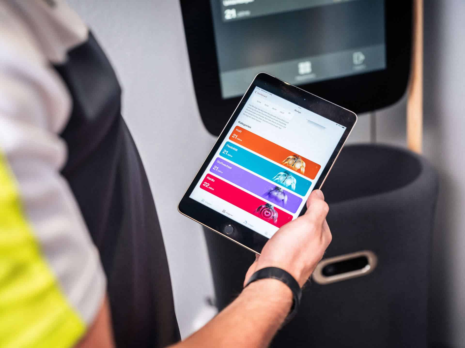 Trainer zeigt die Fitness-Point Member-App auf einem Tablet mit BioAge-Auswertung für Kraft, Flexibilität, Stoffwechsel und Kardio