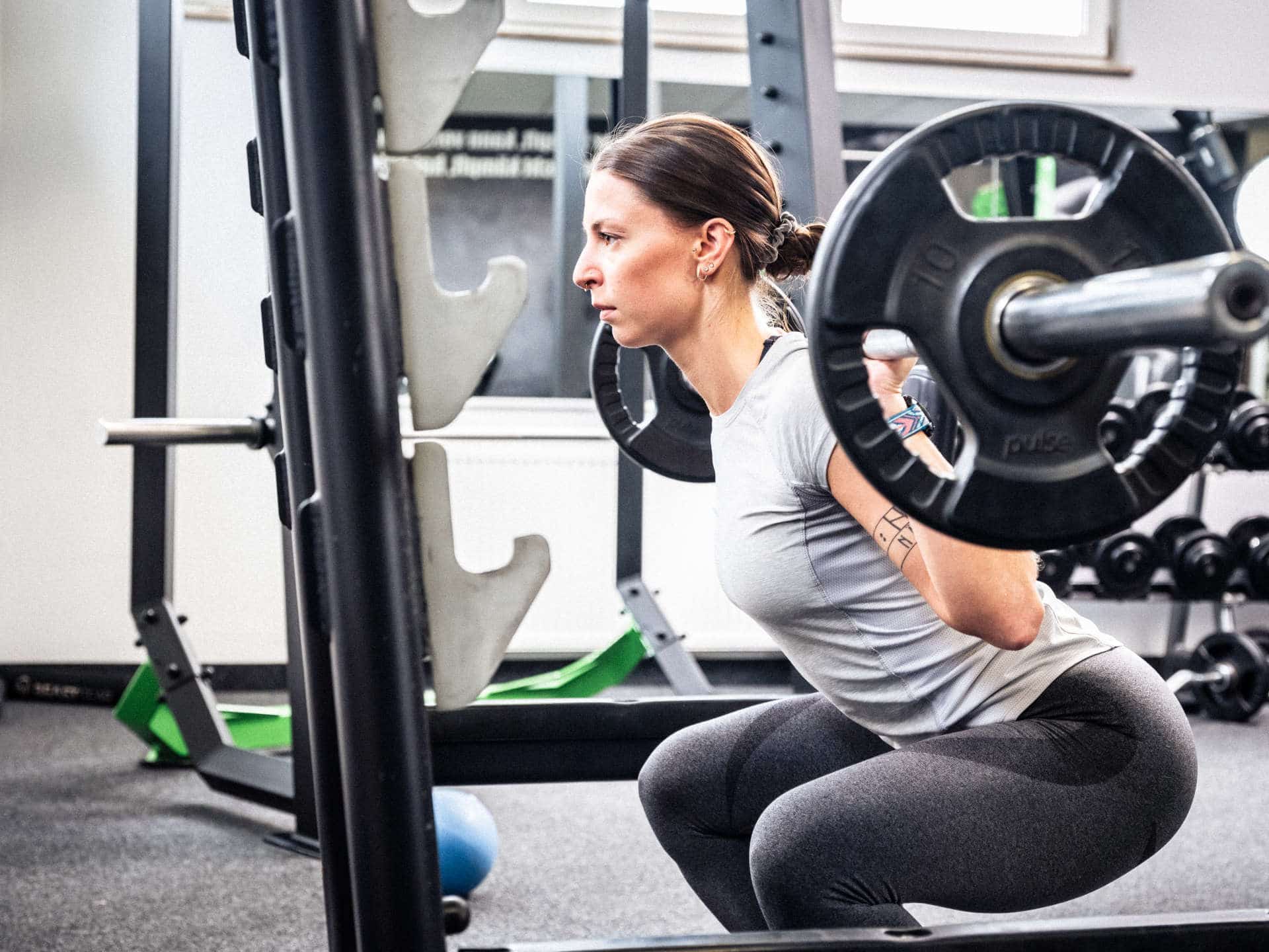 Junge Sportlerin trainiert mit Langhantel im Squat Rack